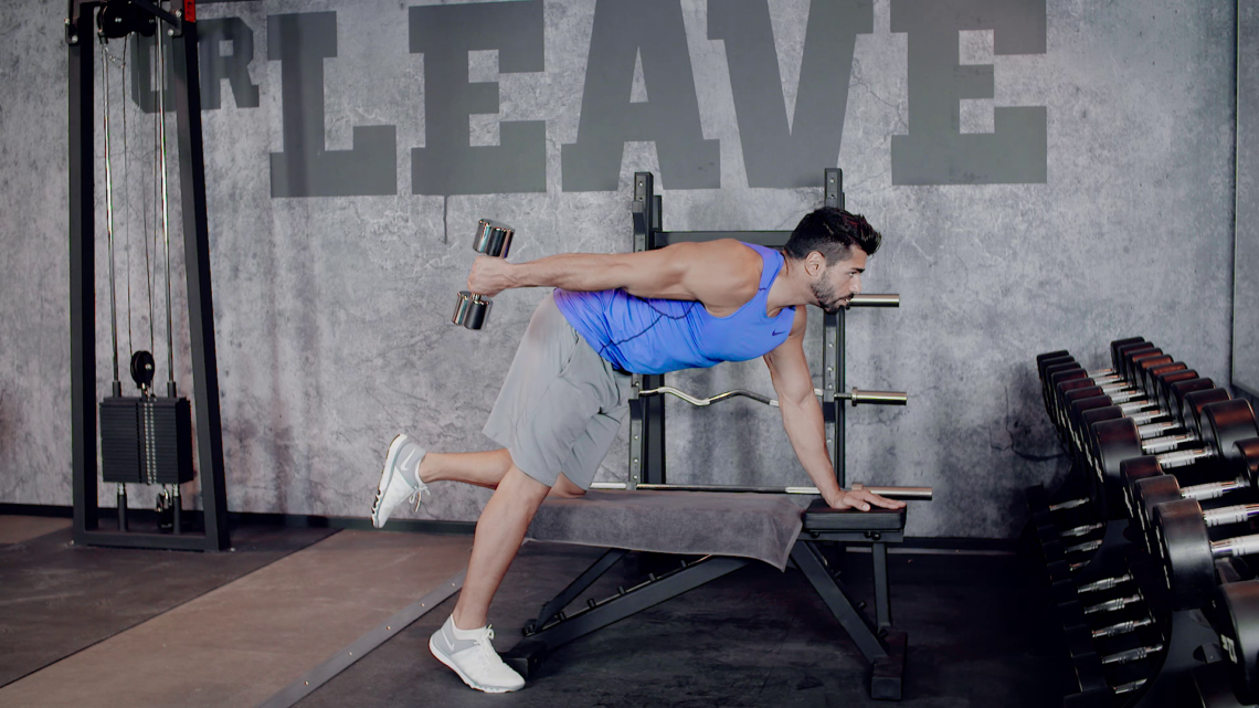 Tricep Kickbacks Mann im Fitnessstudio kniet auf Hantelbank und macht Tricep Kickbacks