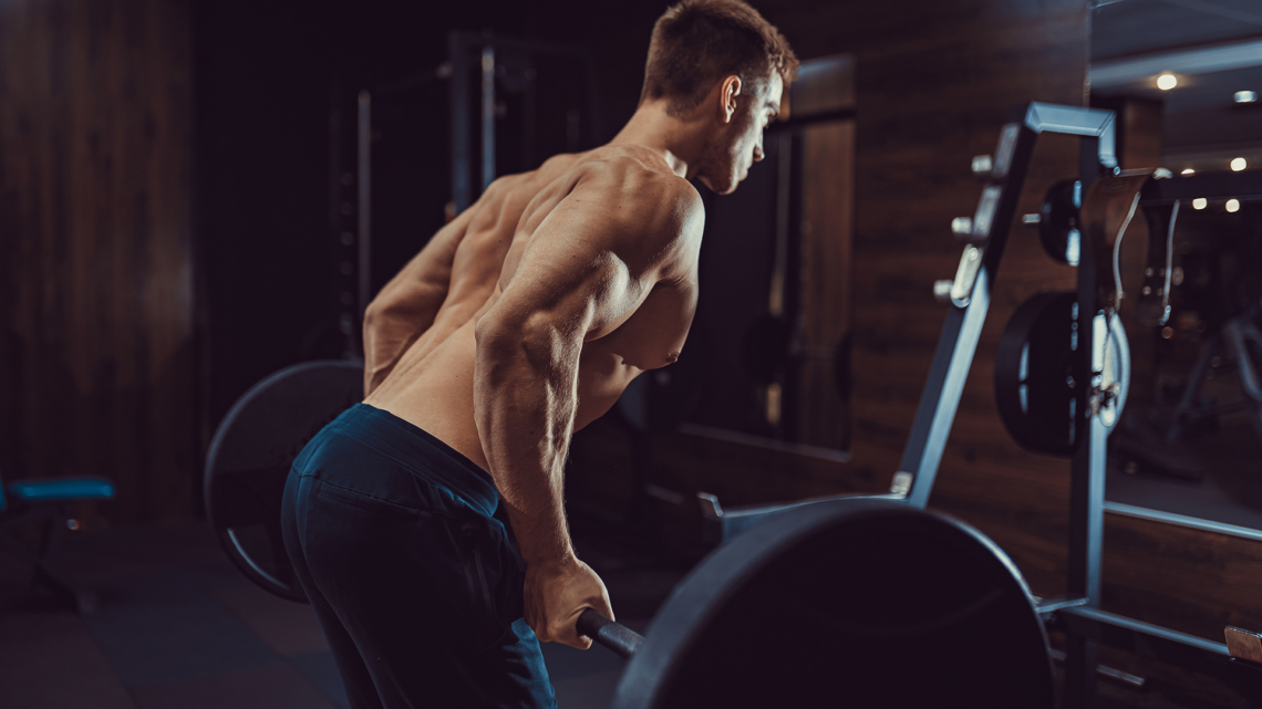 Flacher Bauch Mann beim Langhantel-Rudern im Gym